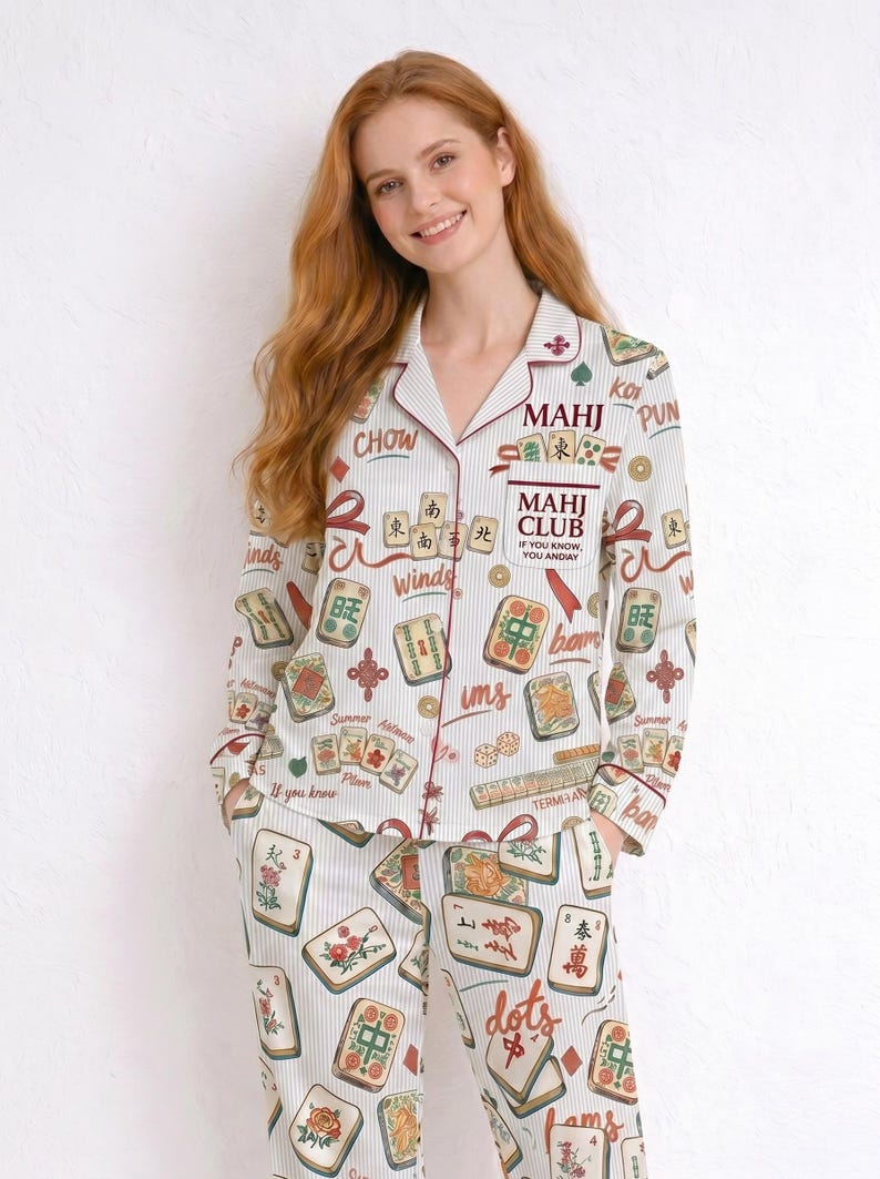 May include: White pajama set with a Mahjong tile print and striped background. The set includes a button-down shirt and pants. The shirt has a burgundy trim and the text "MAHJ CLUB" on the pocket.
