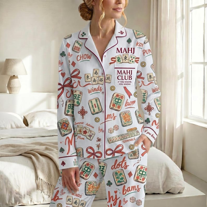 May include: White pajama set with a Mahjong theme. The set features a button-down shirt and pants, adorned with Mahjong tiles, Chinese characters, and the text "MAHJ CLUB". The design includes red accents and ribbon details.