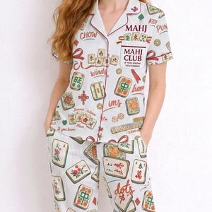 May include: White pajama set with a vertical striped pattern and a Mahjong tile print. The short-sleeved top and pants feature red trim and text including "MAHJ CLUB" and "If you know, you know."