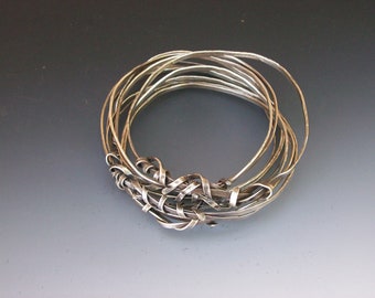 May include: A silver bracelet made of multiple thin, intertwined bands. The bands are twisted and knotted together, creating a unique and intricate design.