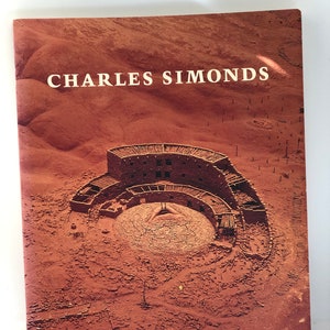 May include: A vintage book cover featuring a photograph of a circular stone structure in a desert landscape. The title "CHARLES SIMONDS" is printed in white letters at the top of the cover.
