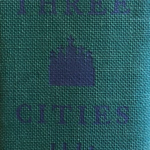 May include: A green fabric book cover with the text "The Cities" and three navy blue crown symbols. The text "1964" is also printed on the cover.