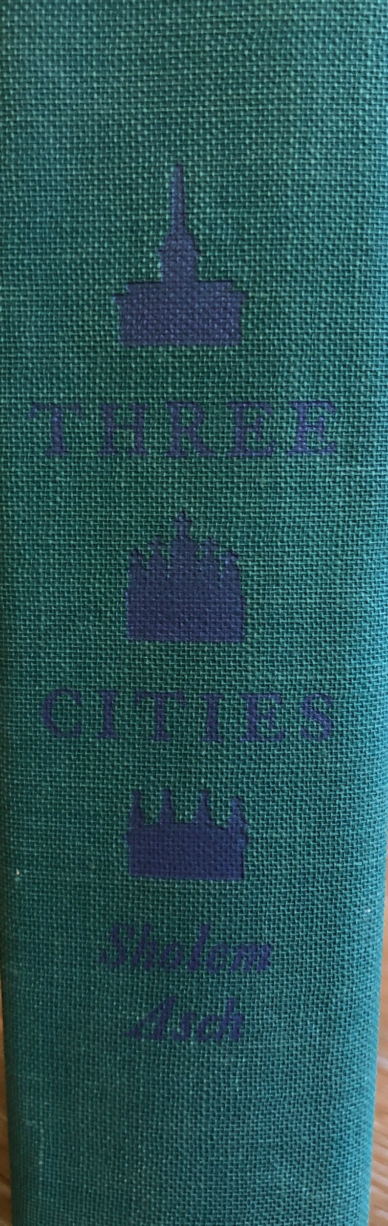 May include: A green fabric book cover with the text "The Cities" and three navy blue crown symbols. The text "1964" is also printed on the cover.