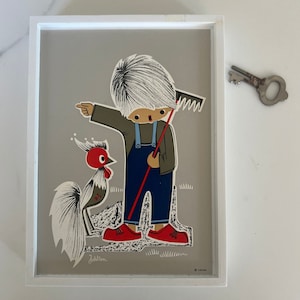 May include: A framed illustration of a boy in overalls holding a rake and a rooster. The boy has white hair and is wearing red shoes. The rooster is gray and white with a red comb. The illustration is on a gray background and is framed in white.