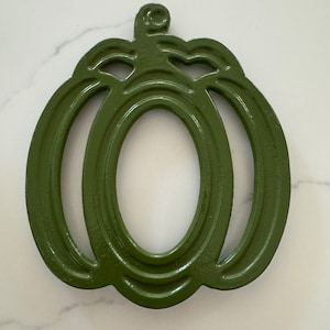 May include: A green cast iron pumpkin-shaped hot pad. The hot pad has a raised design and is perfect for protecting surfaces from hot dishes.