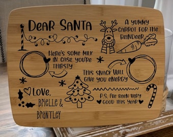 Op de afbeelding: Een houten snijplank met een kerstthema. Het heeft een boodschap voor Sinterklaas, een glas melk, een wortel, een snoepstok en een kerstboom. De tekst luidt: "Lieve Sinterklaas, Hier is wat melk voor je, voor het geval dat je dorst hebt. Een lekkere wortel voor het rendier. Deze snack geeft je energie. Liefs, Brielle & Brantley. P.S. Ik ben dit jaar heel braaf geweest."