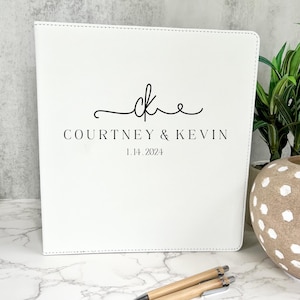 May include: White leather-bound guest book with the initials "CK" and the text "Courtney & Kevin 1.14.2024" in black lettering.
