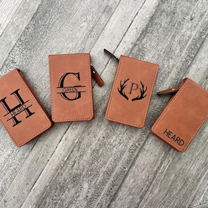 May include: Four brown leather zippered pouches with personalized monograms. The pouches feature the letters "H", "G", "P", and the word "HEARD".