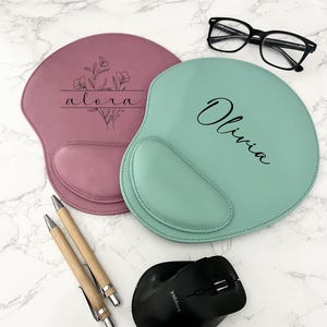 May include: Two personalized wrist rest mouse pads, one pink with the name "alora" and a floral design, and one green with the name "Olivia".