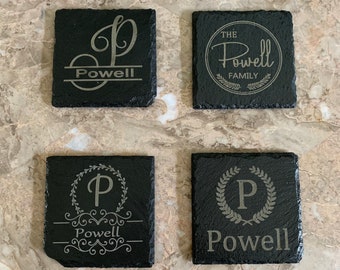 May include: Four black slate coasters with different engraved designs. The coasters feature the letter "P" and the word "Powell" in a variety of styles.