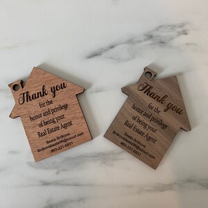 Puede incluir: Dos tarjetas de agradecimiento de madera con forma de casa con el texto "Gracias por el honor y el privilegio de ser su agente inmobiliario" y el nombre y la informaci&oacute;n de contacto de Beata Brdkova.