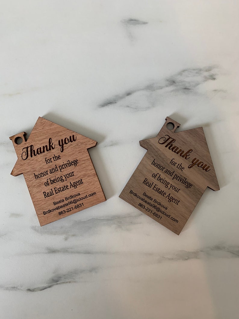 Puede incluir: Dos tarjetas de agradecimiento de madera con forma de casa con el texto "Gracias por el honor y el privilegio de ser su agente inmobiliario" y el nombre y la informaci&oacute;n de contacto de Beata Brdkova.