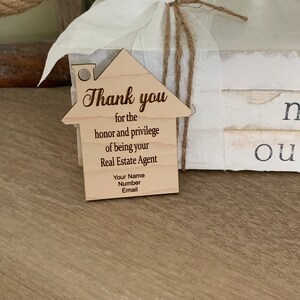 Puede incluir: Una etiqueta de agradecimiento de madera con forma de casa con el texto "Gracias por el honor y el privilegio de ser su agente inmobiliario. Su nombre, n&uacute;mero, correo electr&oacute;nico."