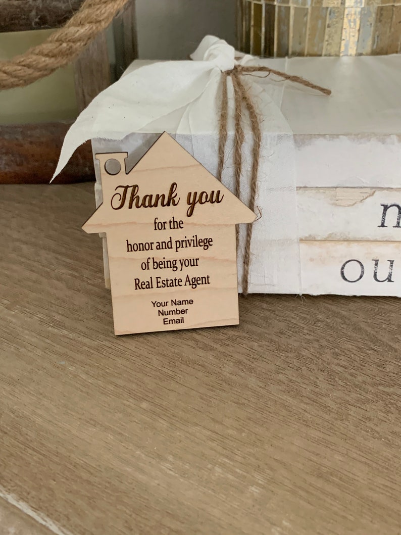 Puede incluir: Una etiqueta de agradecimiento de madera con forma de casa con el texto "Gracias por el honor y el privilegio de ser su agente inmobiliario. Su nombre, n&uacute;mero, correo electr&oacute;nico."