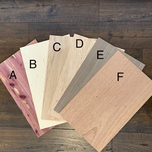 Puede incluir: Seis muestras diferentes de chapa de madera etiquetadas de la A a la F. Las muestras est&aacute;n dispuestas en forma de abanico sobre un suelo de madera oscura. Las chapas de madera son de varios tonos de marr&oacute;n, rojo y blanco.