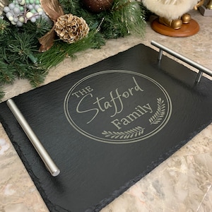 May include: Black slate serving tray with silver handles. The tray has a circular design with the text "The Stafford Family" engraved in a light gray color.
