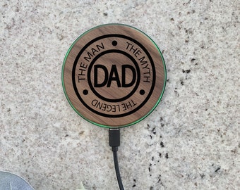 May include: A wooden wireless charging pad with a green LED light ring. The pad has the text "The Man The Myth The Legend" engraved around the edge and "DAD" in the center.
