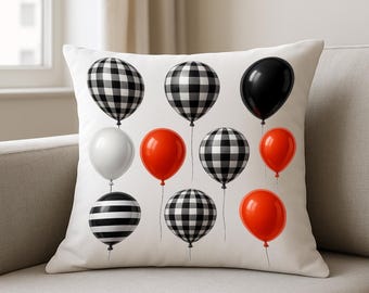Könnte beinhalten: Quadratisches Kissen mit weißem Hintergrund, verziert mit verschiedenen Ballondesigns. Die Ballons sind in schwarz-weiß kariert, schwarz, weiß, rot und schwarz-weiß gestreift. Das Kissen liegt auf einem beigefarbenen Sofa.