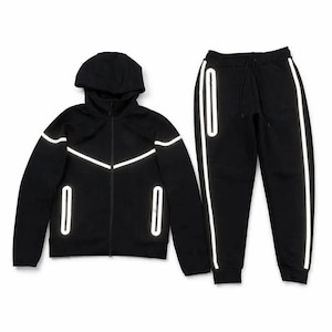 Op de afbeelding: Zwart trainingspak. De set bestaat uit een jack met capuchon en ritssluiting en een bijpassende joggingbroek. Beide items hebben reflecterende witte accenten langs de naden en rond de zakken. De jas heeft een volledige ritssluiting en een capuchon. De joggingbroek heeft een taille met trekkoord.
