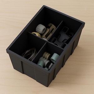 May include: A black plastic organizer with four compartments, filled with various small hardware items in shades of gray, beige, and green. The organizer sits on a light wood surface.