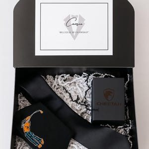 May include: A black gift box containing a black tie with a golf-themed design, a solid black tie, and a small black box with the word "CHEETAH" on it. The box also has a card that says "Canzoa" and "WILL YOU BE MY GROOMSMAN".