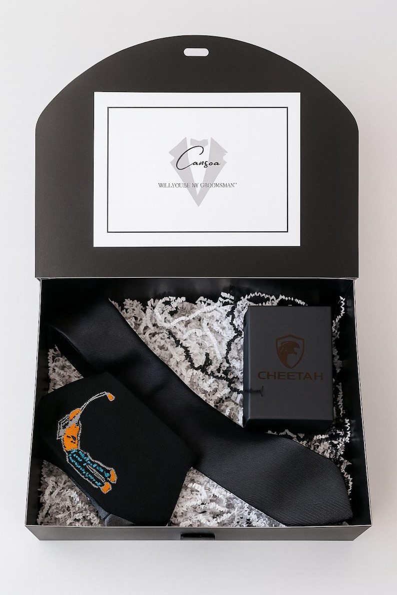 May include: A black gift box containing a black tie with a golf-themed design, a solid black tie, and a small black box with the word "CHEETAH" on it. The box also has a card that says "Canzoa" and "WILL YOU BE MY GROOMSMAN".