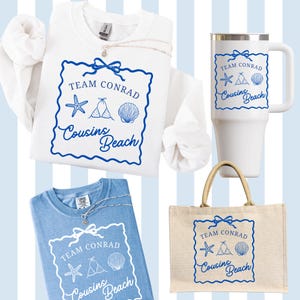 以下が含まれることがあります： 白いスウェットシャツ、青いTシャツ、白いトラベルマグ、ベージュのトートバッグなど、ビーチをテーマにした商品のコレクション。各アイテムには、「Team Conrad」と「Cousins Beach」の文字と、貝殻とヒトデのイラストが描かれた青いグラフィックが施されています。