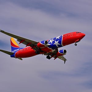 Puede incluir: Un avión de pasajeros de Southwest Airlines en vuelo, con una librea roja, azul y amarilla y un patrón de estrellas blancas en el fuselaje. La aeronave se muestra desde un ángulo bajo contra un cielo nublado, revelando sus alas y motores.
