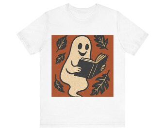 Op de afbeelding: Wit t-shirt met een cartoon geest die een boek leest. De geest is beige met een lachend gezicht, omringd door zwarte bladeren op een oranje achtergrond. Een leuk, griezelig ontwerp voor Halloween of boekenliefhebbers.
