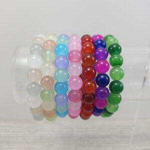 May include: A set of ten bracelets made of round, translucent beads in various colors, including white, light green, light blue, pink, red, purple, and green.