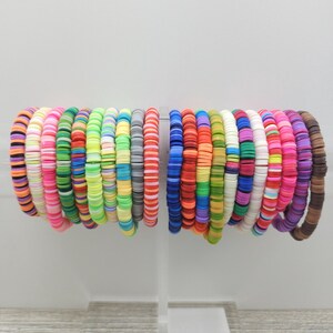 May include: A collection of colorful bracelets made with small, round, plastic beads. The bracelets are stacked together and arranged in a rainbow pattern.