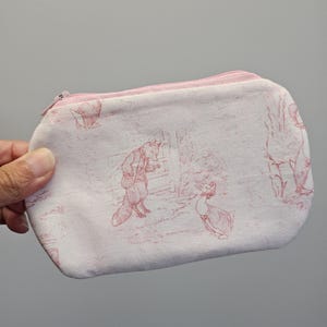 May include: A small, rectangular fabric pouch featuring a light pink background with a repeating red line-art illustration of a fox and a duck. The pouch includes a matching light pink zipper closure along the top edge for securing contents.