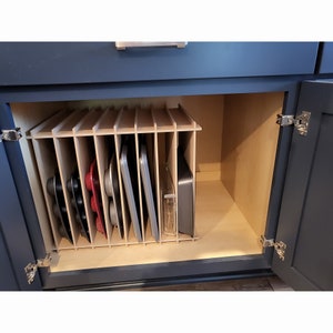 The Steady Hand Kitchen Cabinet Deluxe Muffin Pan Organizer filled with pans in a cabinet.