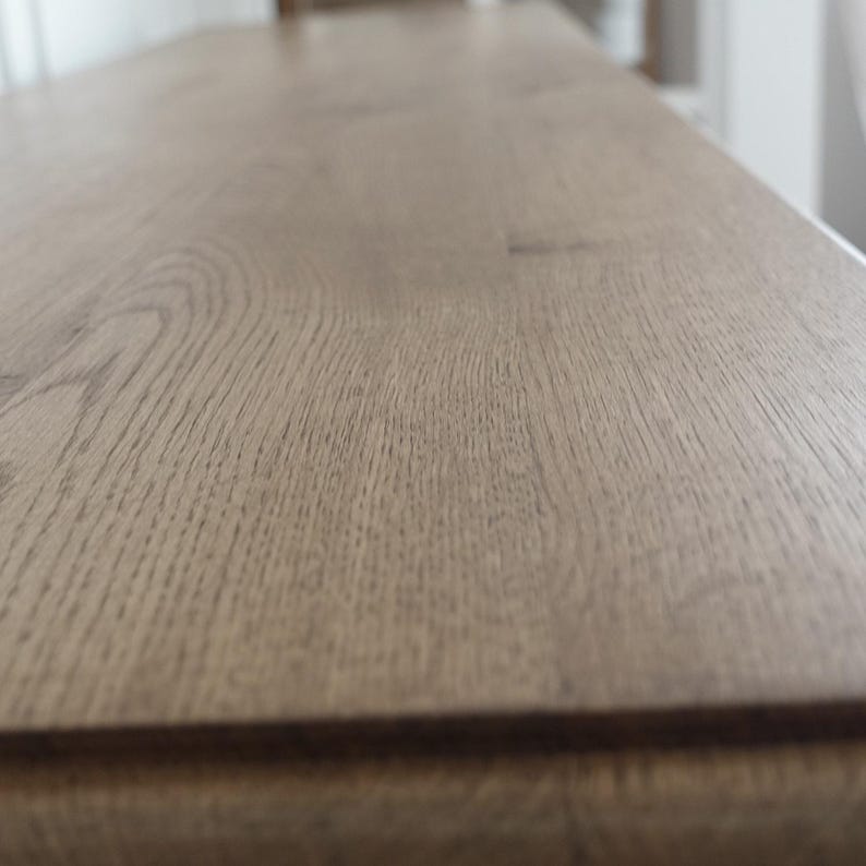 Op de afbeelding: Close-up van een lichtbruin houten oppervlak met zichtbare houtnerf. Het oppervlak lijkt deel uit te maken van een groter meubelstuk, mogelijk een tafel of aanrecht. Het hout heeft een natuurlijke, getextureerde uitstraling.