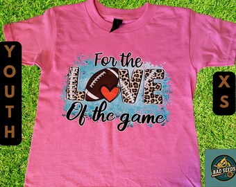 May include: Pink youth t-shirt with the text "For the LOVE of the game" featuring a football and heart graphic. The word "LOVE" has a leopard print design. Includes a size XS tag.