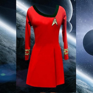 Puede incluir: Un vestido rojo con mangas largas, cuello verde y detalles dorados en los puños. El vestido presenta un emblema dorado y blanco en el pecho. El vestido es un disfraz, probablemente inspirado en un tema de ciencia ficción.
