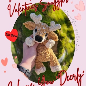 May include: A crocheted deer plush toy in shades of tan and cream, featuring heart-shaped antlers. The image includes the text "Dusk The Valentines Snuggler" and "I Love You Deerly" in red script, plus a red heart with "No Sew".