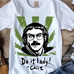 Puede incluir: Camiseta blanca con una ilustración en blanco y negro de un hombre con gafas y bigote, sobre un diseño de explosión verde. El texto "Do it lady! -Chit" está escrito debajo de la ilustración.