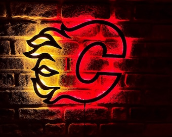 May include: A neon sign featuring the Calgary Flames logo, a stylized 'C' with a flame design. The sign glows red and yellow against a brick wall background, creating a vibrant and eye-catching display.
