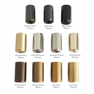 May include: A collection of twelve cylindrical metal hardware knobs arranged in three rows. The finishes include Blackened Brass, Black Brass, Matte Black, Brushed Brass, Polished Chrome, Brushed Chrome, Polished Brass, Antique Patina, and Raw Brass.
