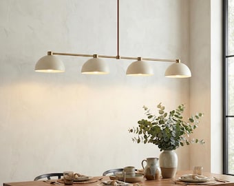 May include: A linear pendant light fixture featuring four matte cream-colored dome shades suspended from a thin, horizontal brass-toned metal rod. The fixture is mounted to the ceiling by a single vertical rod, providing downward illumination.