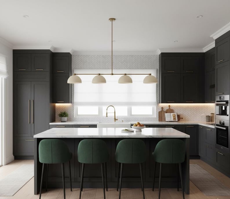 May include: A kitchen featuring dark charcoal cabinetry, a white marble-topped island, and four dark green upholstered stools. A linear brass pendant light with four dome-shaped shades hangs above the island, centered in front of a window.