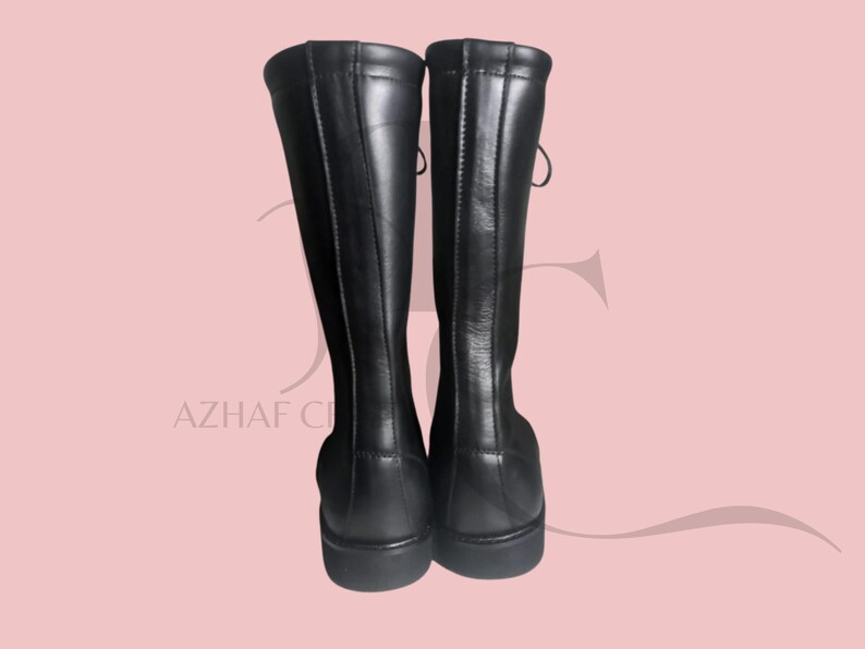 K&ouml;nnte beinhalten: Ein Paar schwarze kniehohe Stiefel. Die Stiefel bestehen aus einem glatten, gl&auml;nzenden Material und haben eine runde Spitze. Die Stiefel haben ein Schn&uuml;rdesign auf der R&uuml;ckseite und einen kleinen Absatz. Die Stiefel werden vor einem hellrosa Hintergrund pr&auml;sentiert.