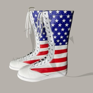 Könnte beinhalten: Paar hohe, weiße Lederstiefel mit patriotischem Design. Die Stiefel zeigen die amerikanische Flagge mit blauen Paneelen, die mit weißen Sternen und roten und weißen Streifen bedeckt sind. Sie haben weiße Schnürsenkel und Sohlen.