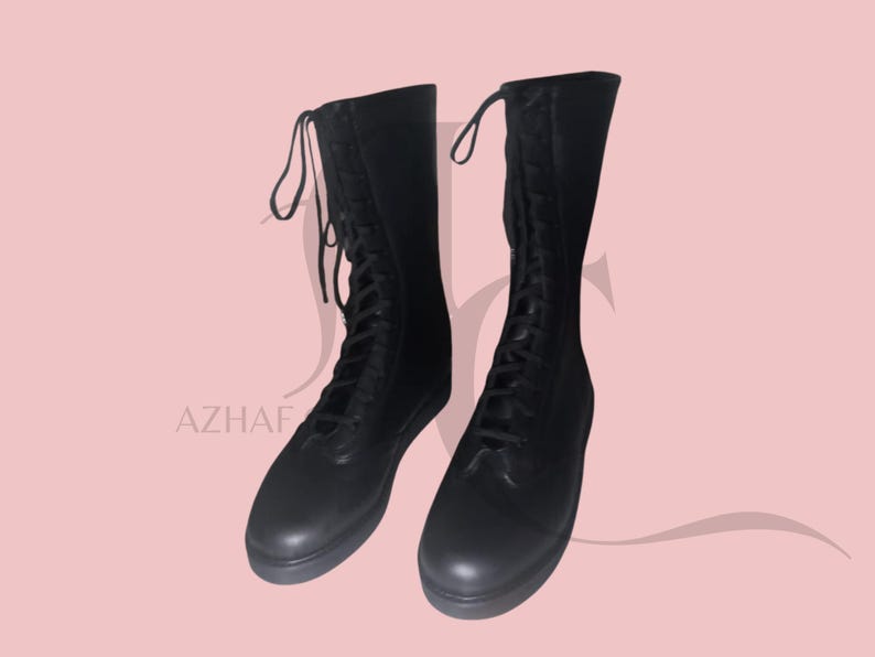 K&ouml;nnte beinhalten: Ein Paar schwarze, kniehohe Stiefel mit Schn&uuml;rdesign. Die Stiefel haben eine runde Spitze und eine glatte, matte Oberfl&auml;che. Die Schn&uuml;rsenkel reichen bis zum oberen Rand des Stiefels. Die Stiefel werden vor einem hellrosa Hintergrund pr&auml;sentiert.