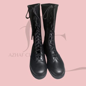 K&ouml;nnte beinhalten: Ein Paar schwarze, kniehohe Stiefel mit Schn&uuml;rdesign. Die Stiefel haben eine runde Spitze und eine robuste Sohle. Die Schn&uuml;rsenkel verlaufen &uuml;ber die Vorderseite der Stiefel, und die Oberseite der Stiefel hat eine Schlaufe zum einfachen Ziehen.