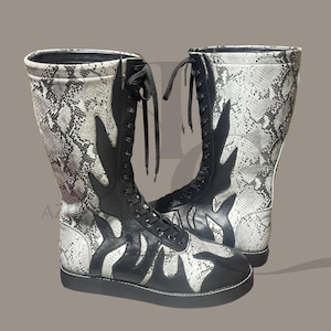 May include: High-top boots featuring a snakeskin pattern in black and white. The boots have black flame-like designs on the sides and a lace-up closure. The soles are black.