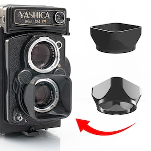 May include: A black Yashica Mat 124 G camera with a lens hood. The camera has a black body with silver accents and a lens that reads f=80mm. Two black lens hoods are shown, one attached and one separate.