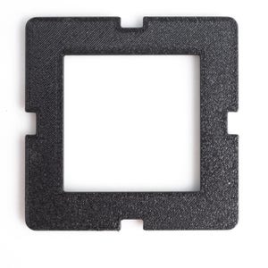 Könnte beinhalten: Ein schwarzer quadratischer Rahmen mit strukturierter Oberfläche und rechteckiger Öffnung. Der Rahmen hat vier Kerben an den Seiten. Der Rahmen ist vor einem weißen Hintergrund platziert.