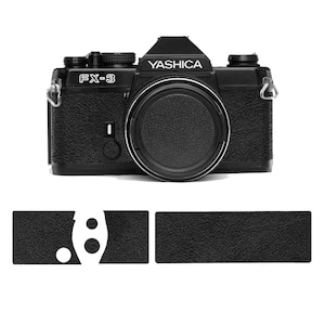 Può includere: Fotocamera Yashica FX-3 nera con copriobiettivo e il nome del marchio stampato in bianco. La fotocamera ha un'impugnatura strutturata e dettagli in metallo argentato. Sotto la fotocamera ci sono tre cuscinetti di presa neri strutturati.